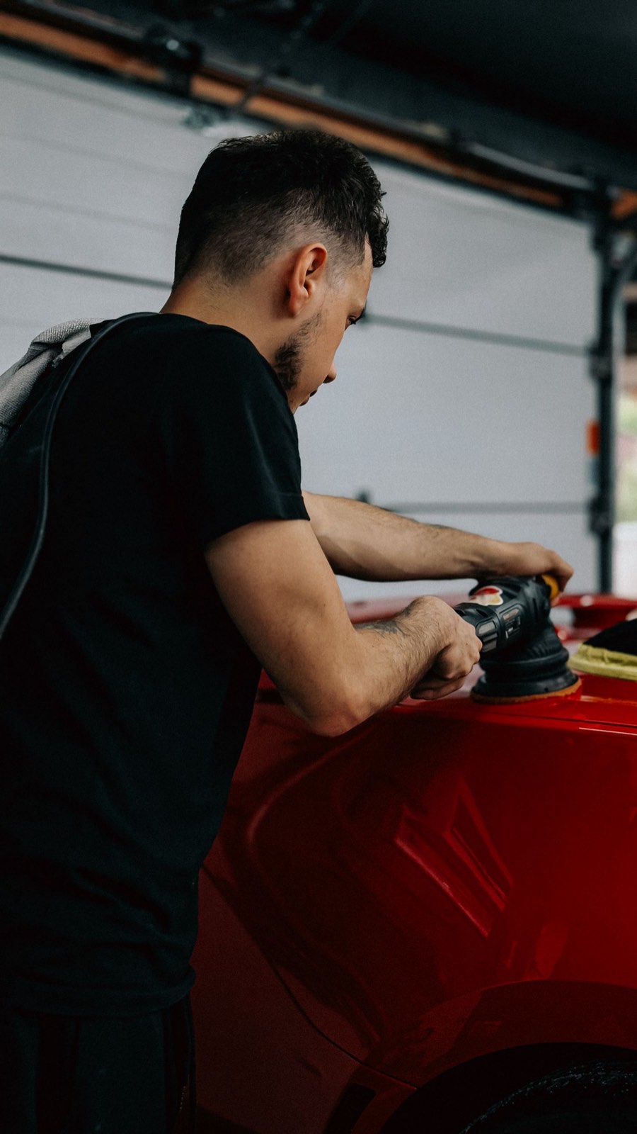 Detailer running a machine polisher over the hood of a red car