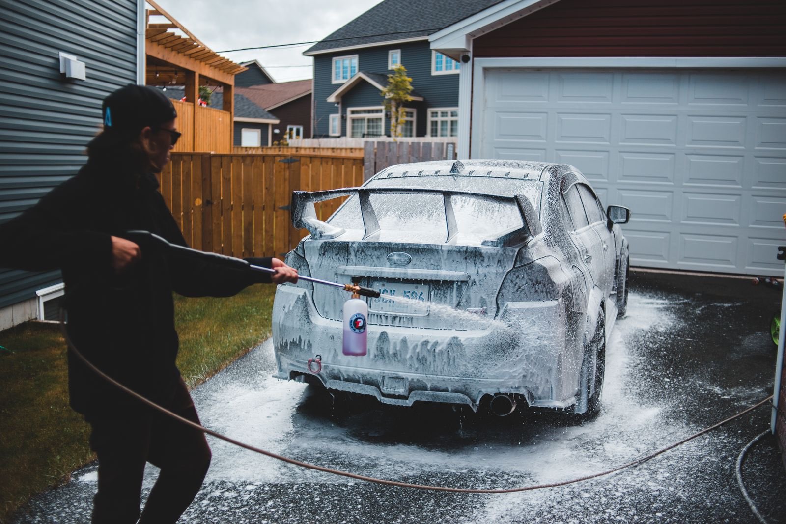 Detailer foaming a car on a home driveway in front of the garage