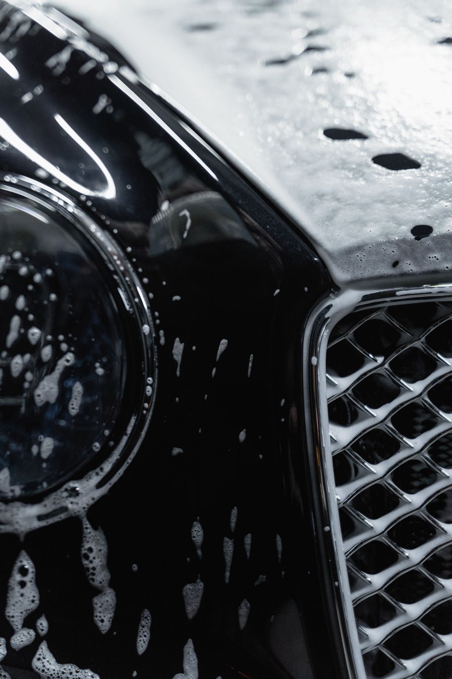 Soap suds rinsing off the front of a black car