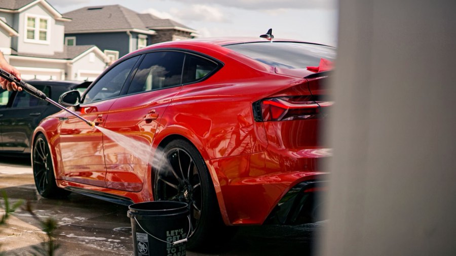 Red car being rinsed in a sunny residential driveway